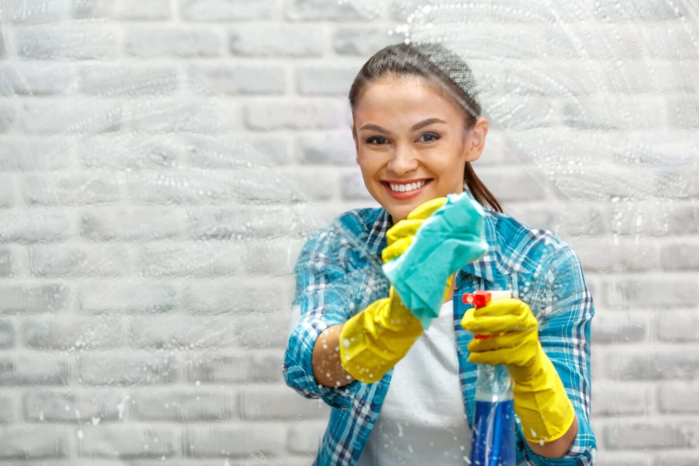 A young woman from the cleaning service smiling at the camera while cleaning the windows