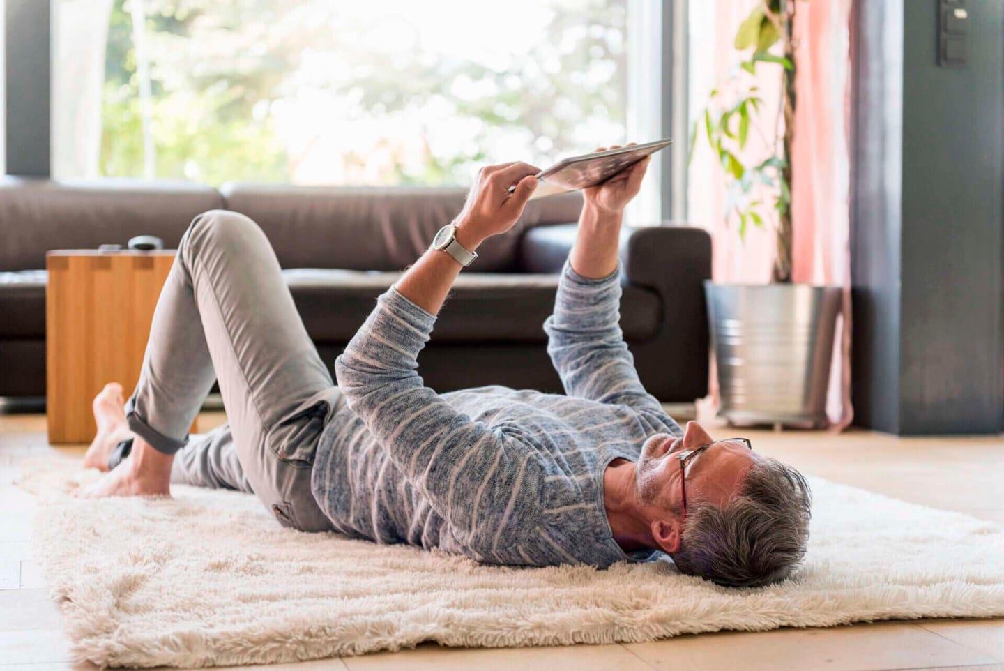 Man lying on a white and cleaned carpet while using a tablet
